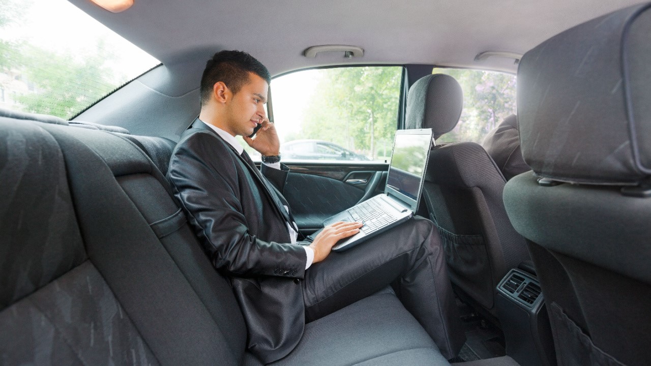 Businessman using laptop and mobile phone while commuting to work by taxi, car
