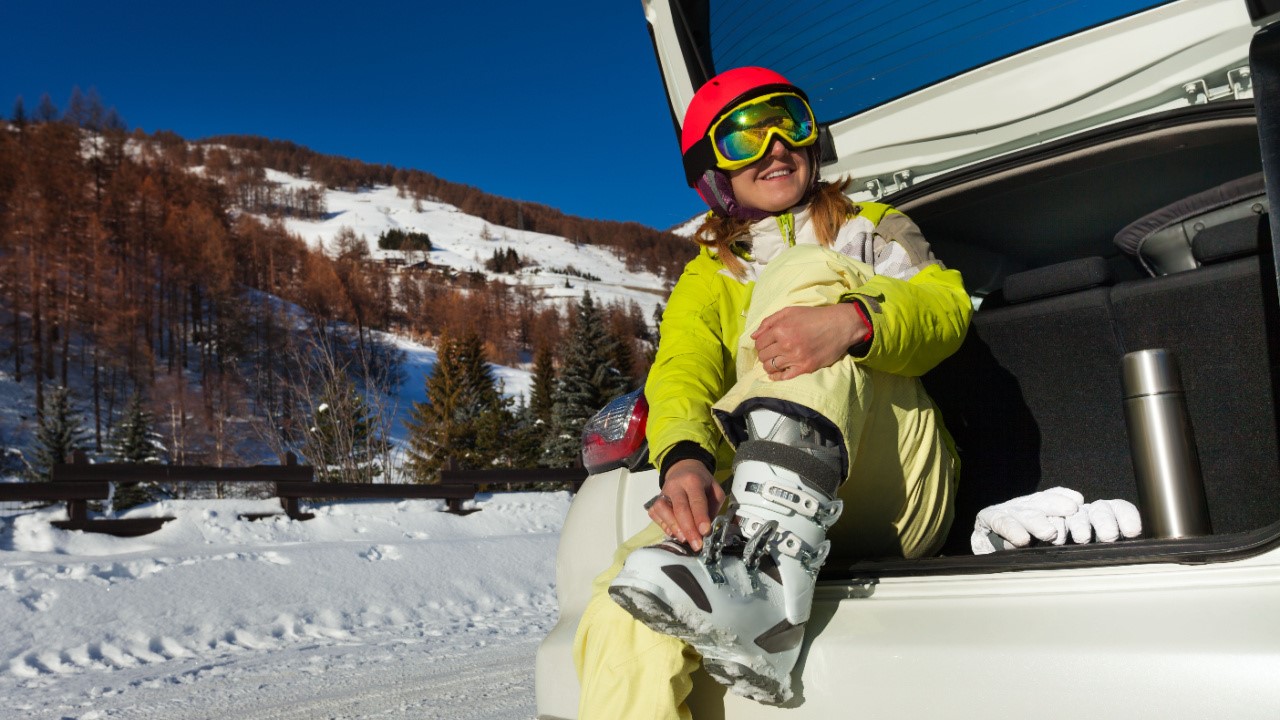 Young woman taking off ski boot after skiing back to her car trunk